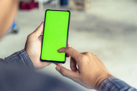 Mockup image of handâ€™s man holding black mobile phone with blank green screen in service...