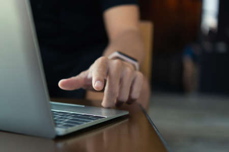 Young man working on his laptop in a coffee shop, front view of business man hands busy using laptop...