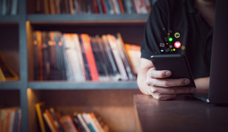 Close up of a business man using cell phone or smartphone with icons in library room background ,Businessman using ,Social, media, Marketing concept /warm retro tone.の写真素材