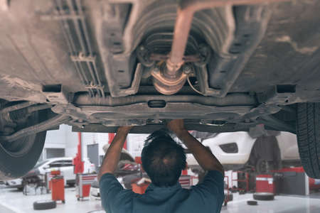 Mid adult mechanic repairing undercarriage of a car in auto repair shop.の写真素材