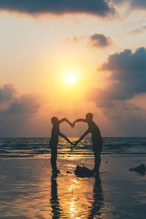 sunset silhouette of young couple in love holding hands at beachの写真素材