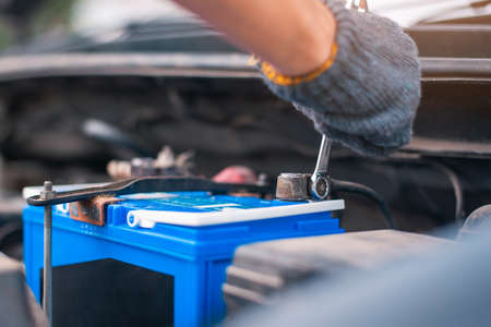 a man tightens with a wrench bolts for fastening a new battery, installing spare parts for a carの写真素材
