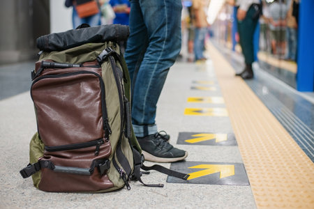 Close up photo of male waiting subway train on platform. Well-dressed handsome man in black sneakers and jeans with backpack in hand standing on station. Modern citizen of big city. Lifestyle concept.の写真素材
