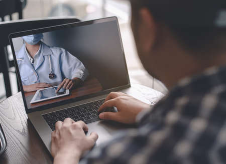 Back view of young man making video call with her doctor while staying at cafe or home. Close up of patient in video conferencing with general practitioner on digital tablet. Sick man in online consultation.の写真素材