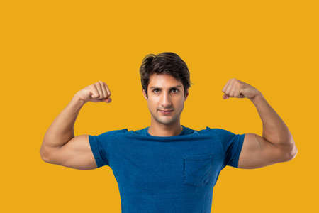 Fit and muscular man flexing his biceps on yellow backgroundの写真素材