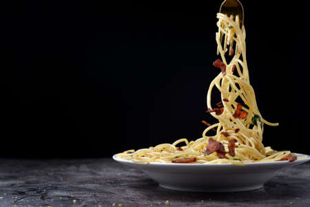 Spicy spaghetti with chilli and bacon, tastly food. Some of spagetti roll on the stainless fork on white plate, copy space for text.の写真素材