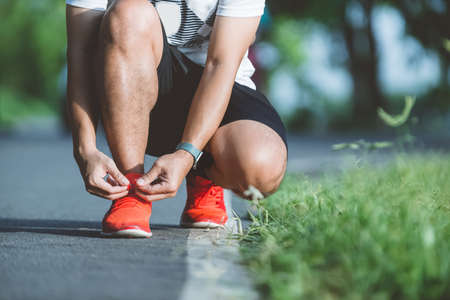 Running shoes runner man tying laces for autumn run in forest park. Runner trying running shoes getting ready for run. Jogging men exercise motivation heatlh and fitness.の写真素材