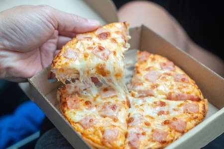 Man eats pizza in his car. Eat takeaway food in the car. Due to closed restaurants during the pandemic, you are forced to order food. Flatbread in a cardboard box.の写真素材