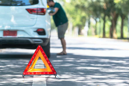 Red warning triangle with a broken down car,Emergency triangle on the road, stopped car and man calling by phone in the background.の写真素材