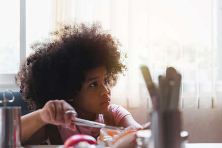 Little african girl holding an artificial model of human jaw with dental braces in orthodontic office, smiling. Pediatric dentistry, aesthetic dentistry, early education and prevention concept.の写真素材