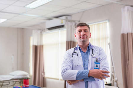 Confident smiling doctor posing and looking at camera with arms crossed, medical staff working on...