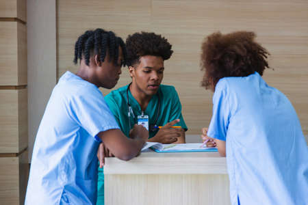 Group of American - African ethnicity medical student or intern doctor in general hospital making a discussion together about symptomatic treatment, happy medical student talking. Healthcare worker.の写真素材