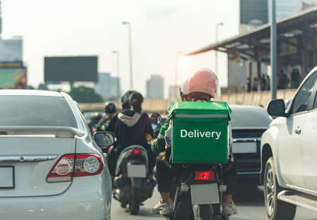 A food delivery driver is driving deliveries to customers ordering food online in a busy capital city.の写真素材
