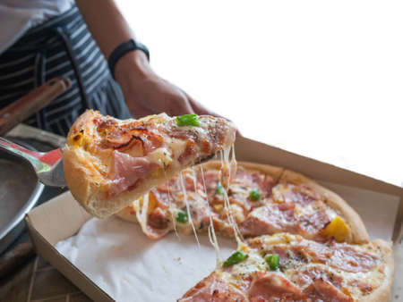 Large slices of hot cheese pizza for lunch or dinner, Hawaiian bacon and bell pepper sauce, delicious Italian fast food on a wooden table.の写真素材
