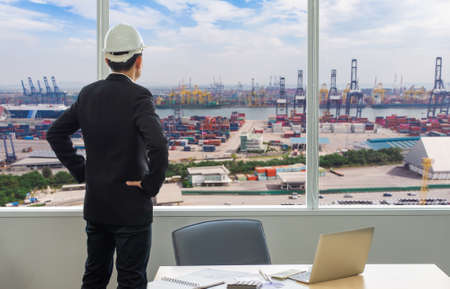 Businessman standing at a port of its own, Back view of a young confident man financier is thinking about something, while is standing outdoors against sea port.の写真素材