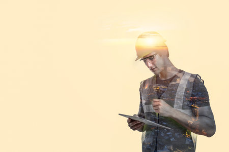 building worker in a double exposure holding a tablet computer while standing in front of an imaginary city building site.の写真素材