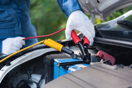a mechanic using jumper cables to manually power a car's batteryの写真素材