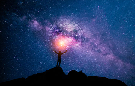 A standing man on a mountain with his hands raised and the night sky filled with stars and the universe. View of the Milky Way.の写真素材