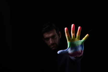 on a dark background, a close-up of a person holding the rainbow pride flag in front of their face.