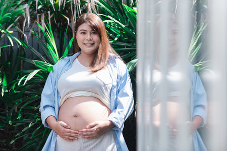 Lovely pregnant Asian woman in the park enjoying the morning sunshine and feeling content