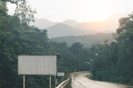 An empty billboard stands by a winding road amidst foggy mountain scenery, signaling potential for advertising.の写真素材