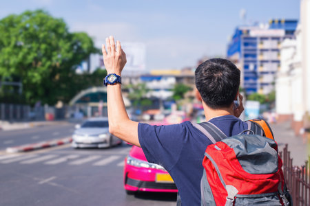 Back view of a man with a backpack and a watch hailing a taxi on a bustling city street.の写真素材