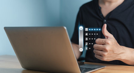 A person shows a thumbs-up gesture beside a five-star rating system on a laptop screen, indicating...
