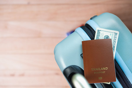 A Thailand passport and US dollar bills placed on a light blue suitcase, symbolizing travel, tourism, international trips, and financial preparedness.の写真素材