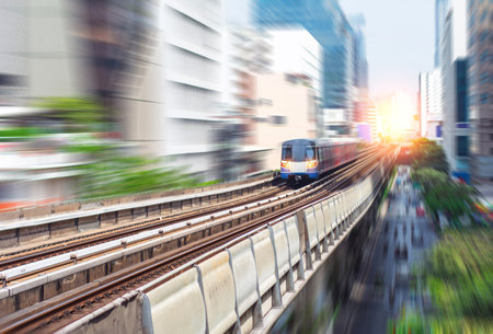 A high-speed electric train travels on elevated tracks through a city during sunset, symbolizing fast, modern urban transportation.の写真素材