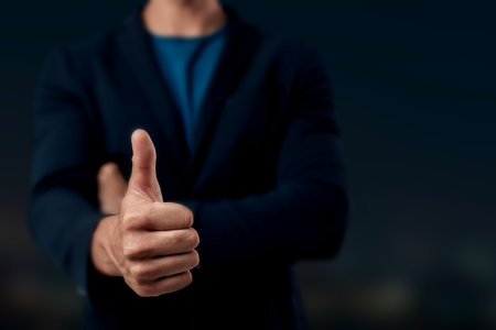 Close-up of a man in dark clothing showing a thumbs up gesture, symbolizing approval, positivity, or encouragement.の写真素材