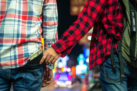 A thief secretly steals a wallet filled with cash from a man's back pocket on a crowded city street at night, highlighting urban crime and public safety issues.の写真素材