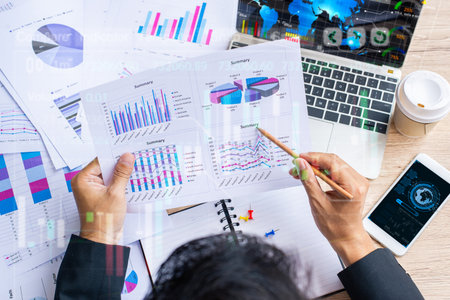 Professional businessman reviewing financial graphs, charts, and investment reports with laptop,...