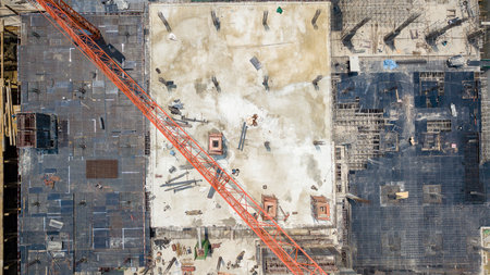 Drone photo of a large concrete construction site showing steel framework, workers, and a red crane arm spanning the project area.の写真素材