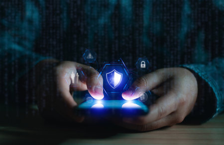 Close-up of hands holding a smartphone displaying a virtual security shield. Concept of mobile data protection, antivirus, and secure online access against cyber attacks.の写真素材