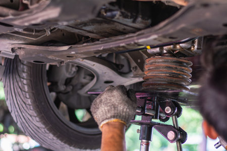 Close-up of a mechanic's gloved hand using a jack to support engine or suspension components while working underneath a car in a garage.の写真素材