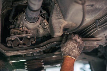 A professional technician checking the transmission housing, rubber mounts, and driveshaft under a vehicle during a routine maintenance inspection.の写真素材