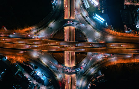 Stunning top-down aerial view of a complex highway interchange at night, featuring vibrant...