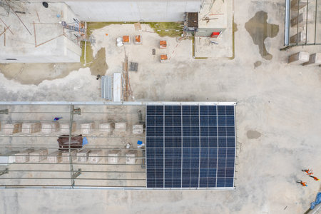High-angle drone shot of a construction site showing workers and solar panels being installed on a metal roof structure.の写真素材