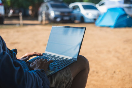 Close-up of a man using a laptop at a campsite. Concept of digital nomad, remote work, and enjoying a vacation in nature.の写真素材