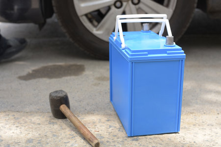 New blue car battery and mallet on the ground prepared for vehicle maintenance or replacement near a car wheel.の写真素材