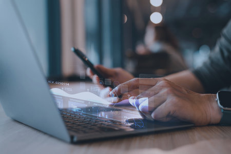 Close-up of man hands using laptop and smartphone with digital business data overlay. Concept of Artificial Intelligence, IoT, and financial technology.の写真素材