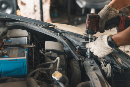 Close-up of mechanic's hands using a cordless impact wrench to repair a car engine. Professional...