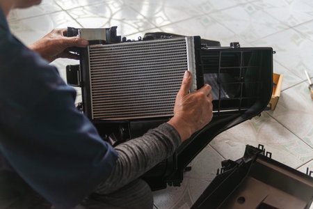 Close-up of a mechanic's hands assembling a new aluminum cooling coil into the car A/C housing unit during maintenance repair.の写真素材