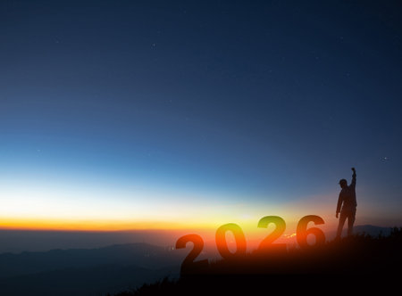 Silhouette of a man standing on a mountain peak with 2026 numbers against a sunrise sky, celebrating success, victory, and new year goals.の写真素材