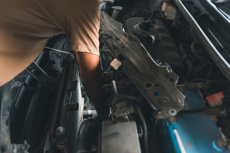 A close-up view of an auto mechanic leaning into the engine bay of a vehicle to check and repair the radiator cooling system.の写真素材
