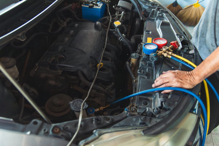 A close-up view of an auto mechanic's hands using a manifold gauge set to test and recharge the air conditioning system in a car's engine bay.の写真素材