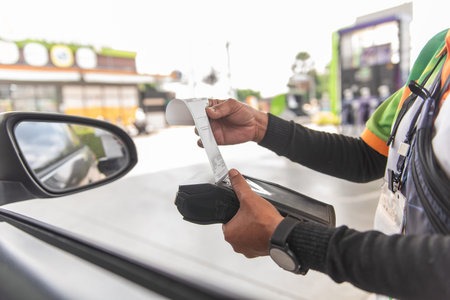 Close-up of a gas station worker holding a mobile payment terminal and pulling out a paper receipt for a customer at a petrol station pump.の写真素材