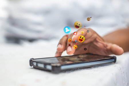 Person browsing social media on a smartphone with animated like, heart, and smile emojis popping up from the screen. Concept of digital marketing and online engagement.の写真素材