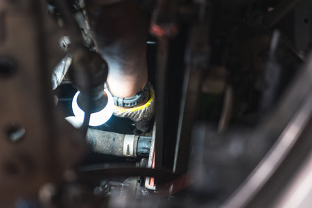 Close up of an auto mechanic wearing gloves, holding a bright work light to inspect the radiator and hoses inside a car engine bay. Auto repair concept.の写真素材