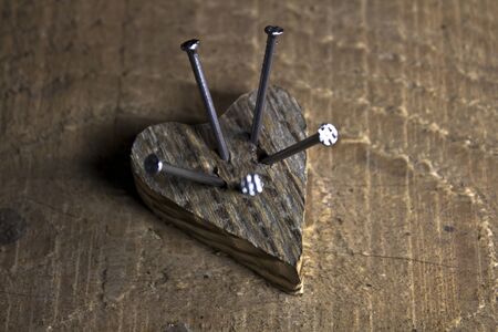 Wooden love heart pierced by nailes on wooden backgroundの写真素材
